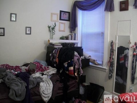 A messy bedroom with a bed covered in clothes and a mirror on the wall.