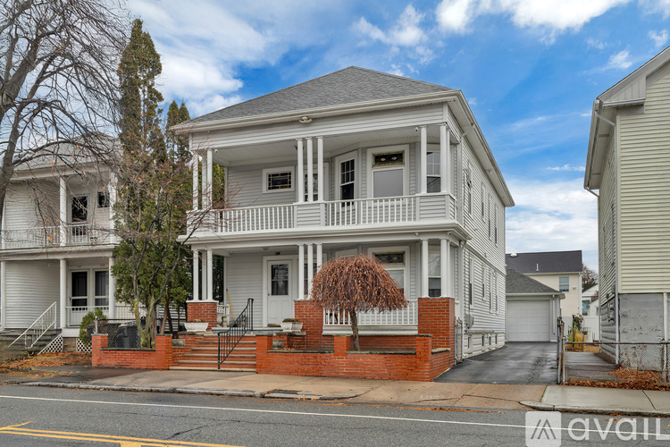 A two-story house with a front porch and a small tree in front.