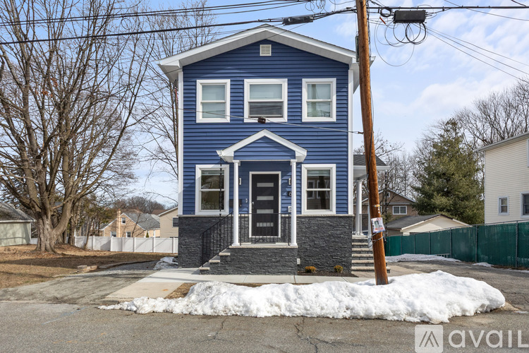 A blue house with a white door and windows is in front of a fence and trees.