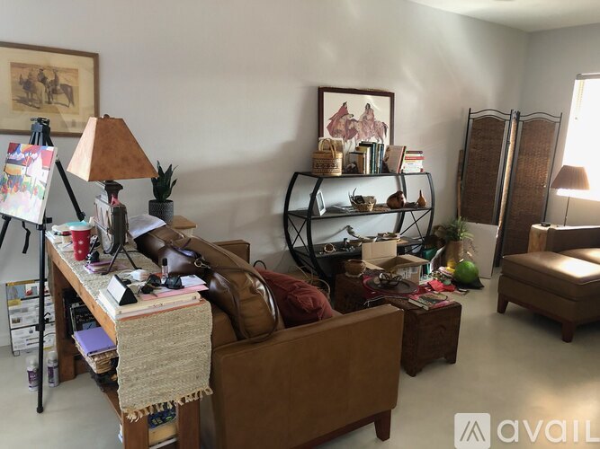 A living room with a brown couch, a table with a lamp and a painting, and a shelf with various items.
