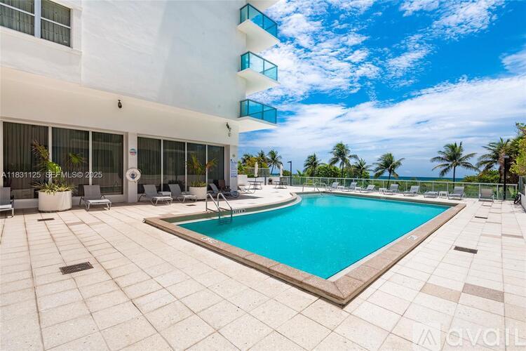 A large swimming pool is surrounded by a patio and a white building with balconies.