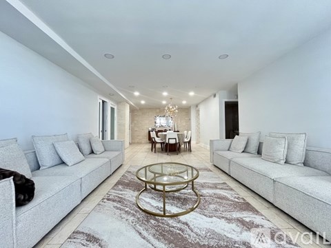A spacious living room with a glass coffee table in the middle.