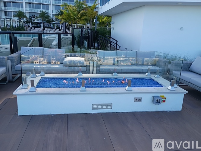 A hot tub on a wooden deck with a white wall and a glass railing in the background.