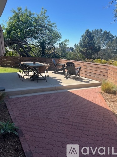 A patio with a table and chairs is surrounded by a brick walkway and a wooden fence.