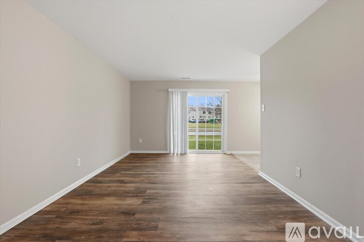A spacious room with wooden flooring and a sliding glass door leading to a balcony.
