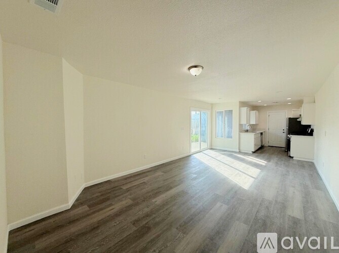 A spacious living room with wood flooring and a kitchen area in the background.