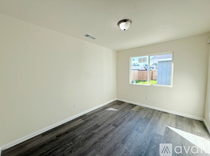 A room with a window showing a view of a fence and a building outside.