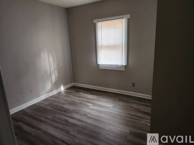 A room with wooden flooring and a window with blinds.