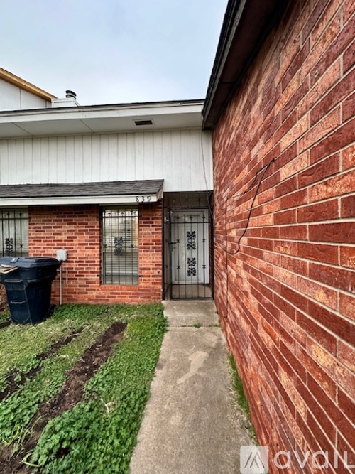 A red brick house with a black trash bin in front.