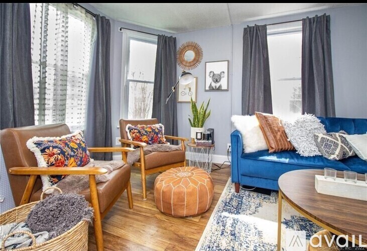 A living room with a blue couch, wooden chairs, and a round ottoman.