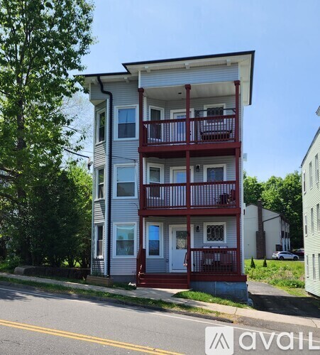 A two-story building with a red balcony is situated on a street.