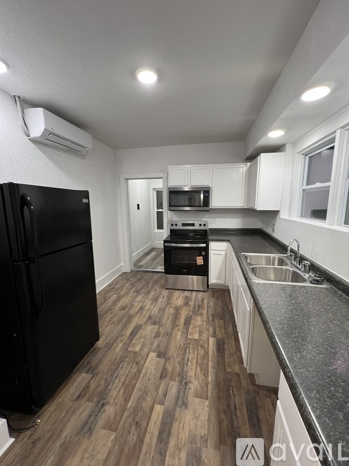 A kitchen with a black fridge and wooden floors.