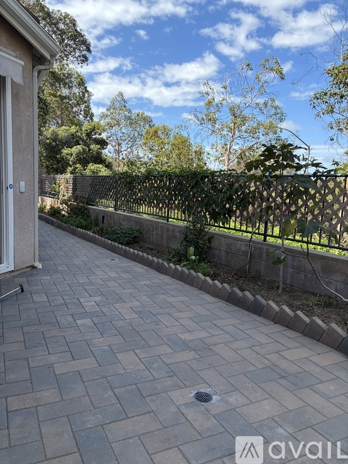 A patio with a brick pattern is surrounded by a fence and trees.