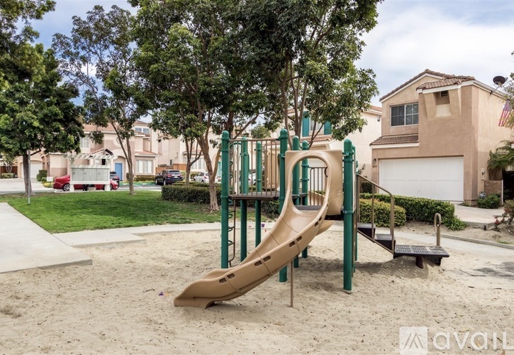 A playground with a slide and sandbox in front of a residential area.