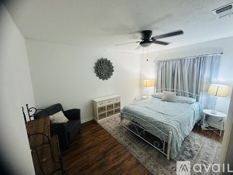 A bedroom with a bed, chair, and ceiling fan.