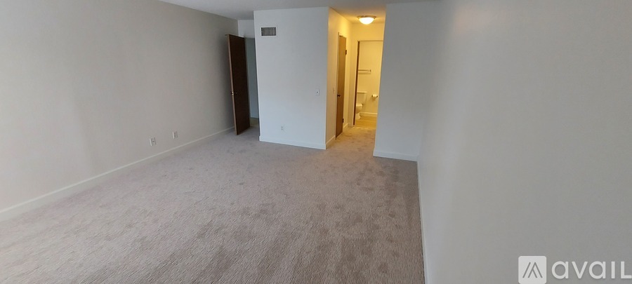 A room with carpeted floor and white walls, with a doorway leading to another room.