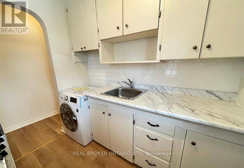 A white washing machine is in a kitchen with white cabinets.