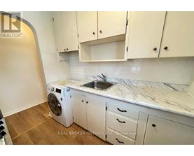 A white washing machine is in a kitchen with white cabinets.