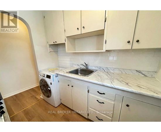 A white washing machine is in a kitchen with white cabinets.