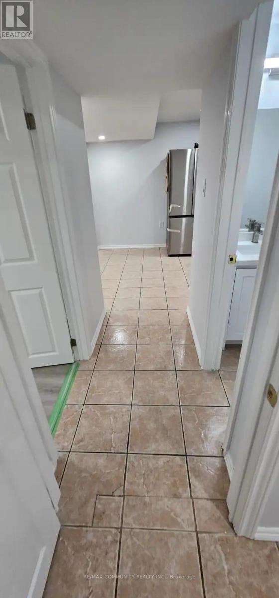 A hallway with a tiled floor and a refrigerator in the background.
