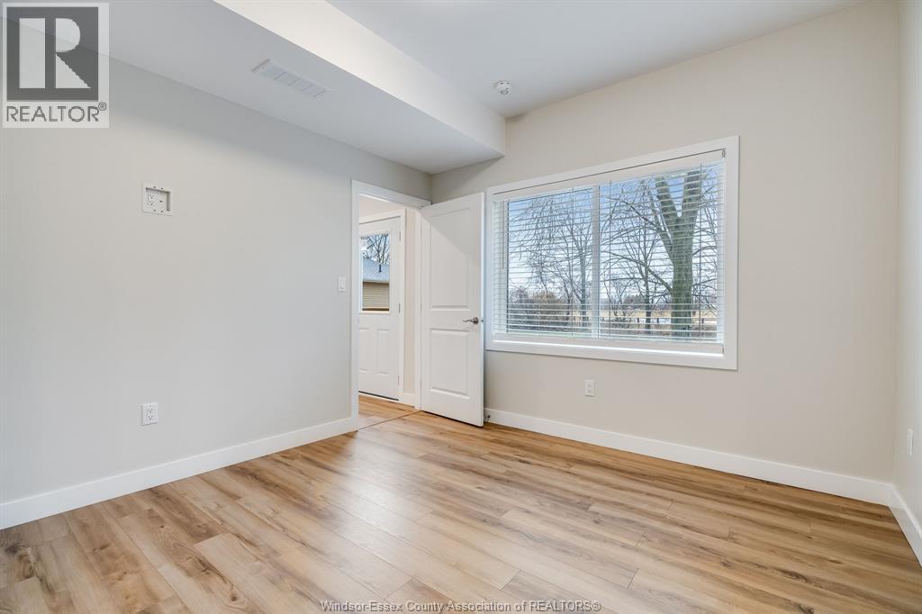 A room with wooden flooring and a large window with a view of trees outside.