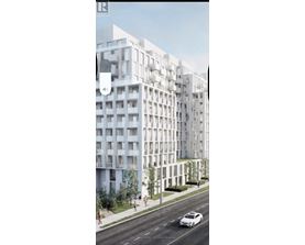 A white car is driving on a road next to a tall white building.