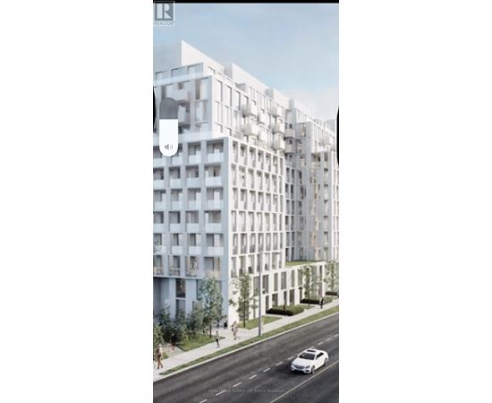 A white car is driving on a road next to a tall white building.