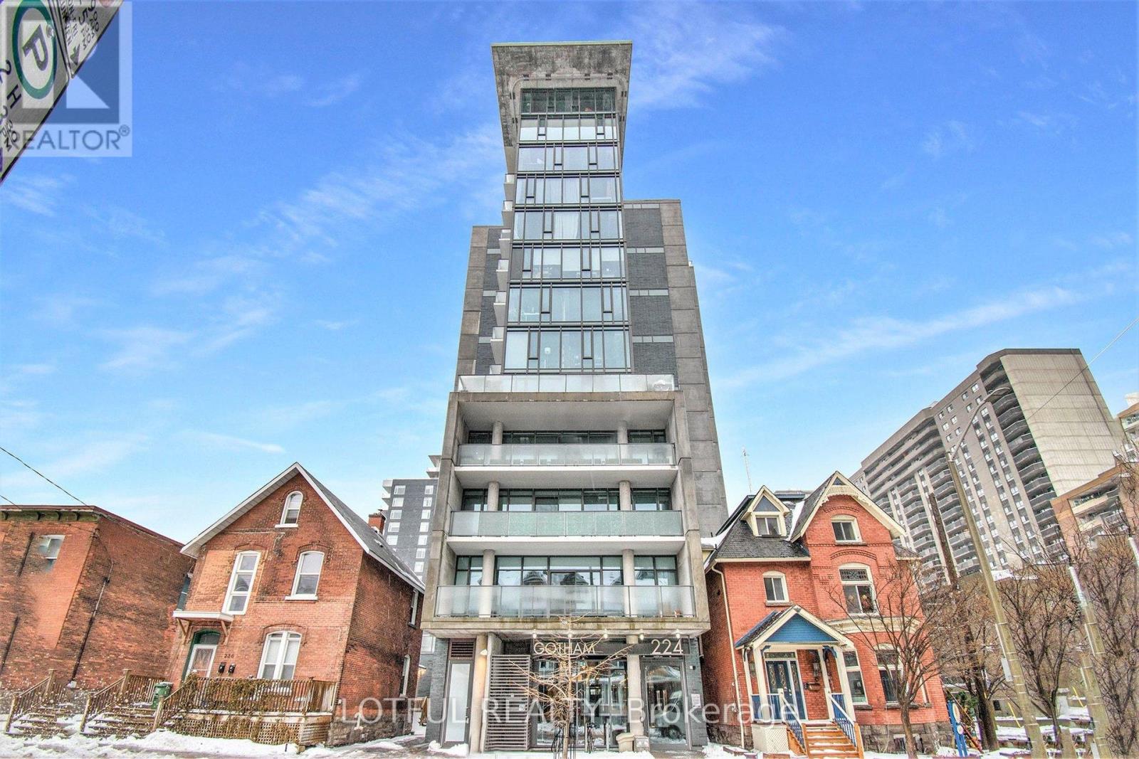 A tall building with a glass facade stands in front of a row of older brick houses.