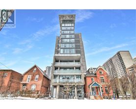 A tall building with a glass facade stands in front of a row of older brick houses.
