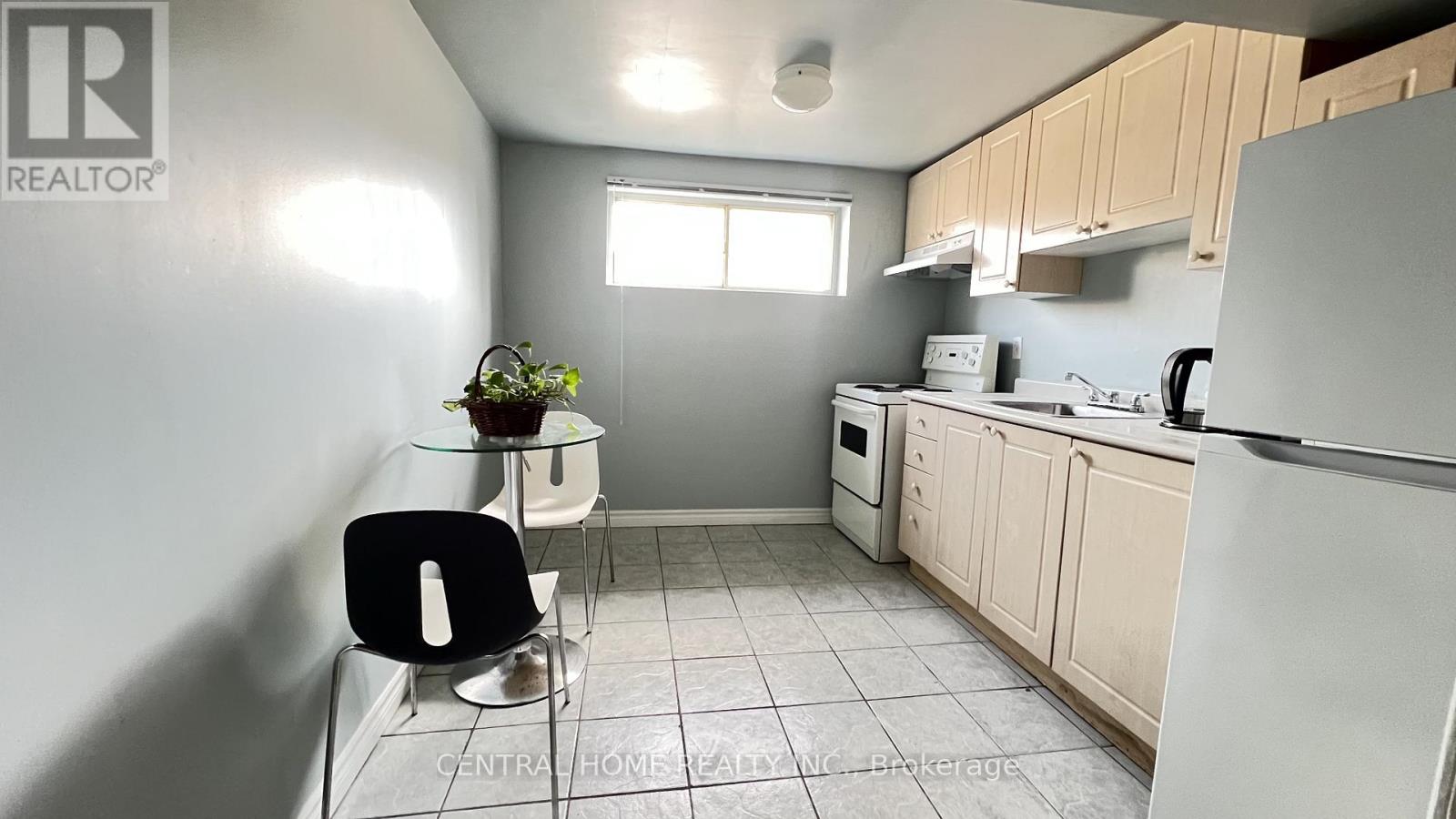 A kitchen with a white fridge, black chair and a plant on the counter.