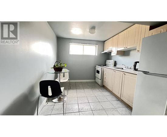 A kitchen with a white fridge, black chair and a plant on the counter.