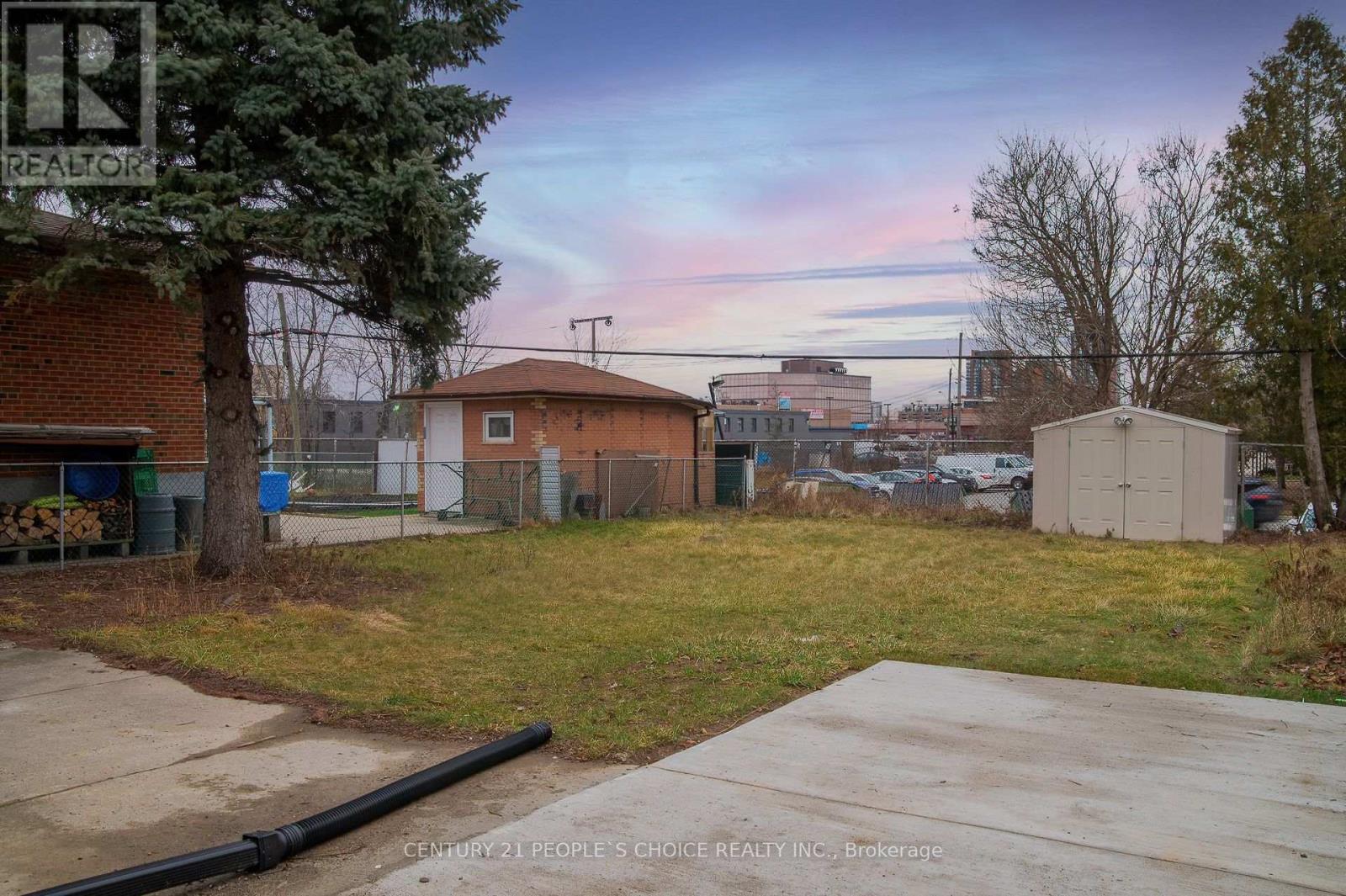 A realtor sign is in the foreground of a grassy lot with a building in the background.