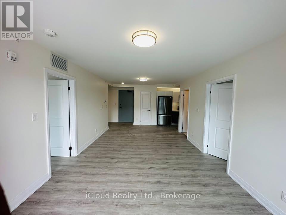 A spacious room with a door on the left and a kitchen area with a refrigerator and cabinets on the right.