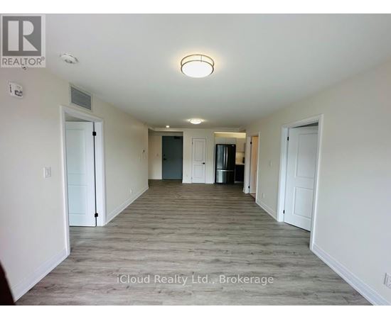 A spacious room with a door on the left and a kitchen area with a refrigerator and cabinets on the right.