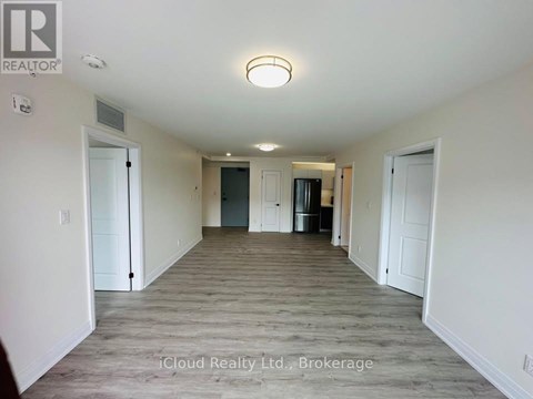 A spacious room with a door on the left and a kitchen area with a refrigerator and cabinets on the right.