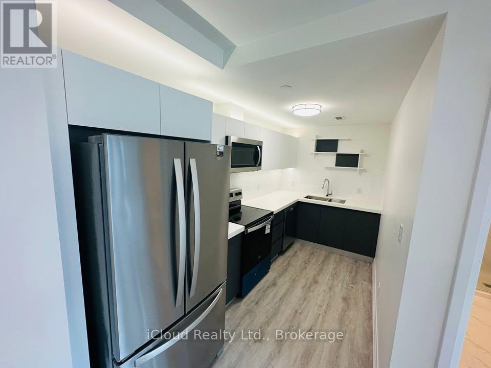 A modern kitchen with a stainless steel refrigerator and wooden flooring.