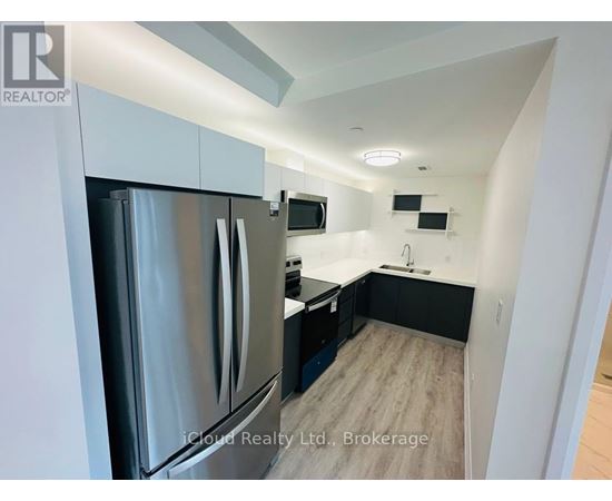A modern kitchen with a stainless steel refrigerator and wooden flooring.