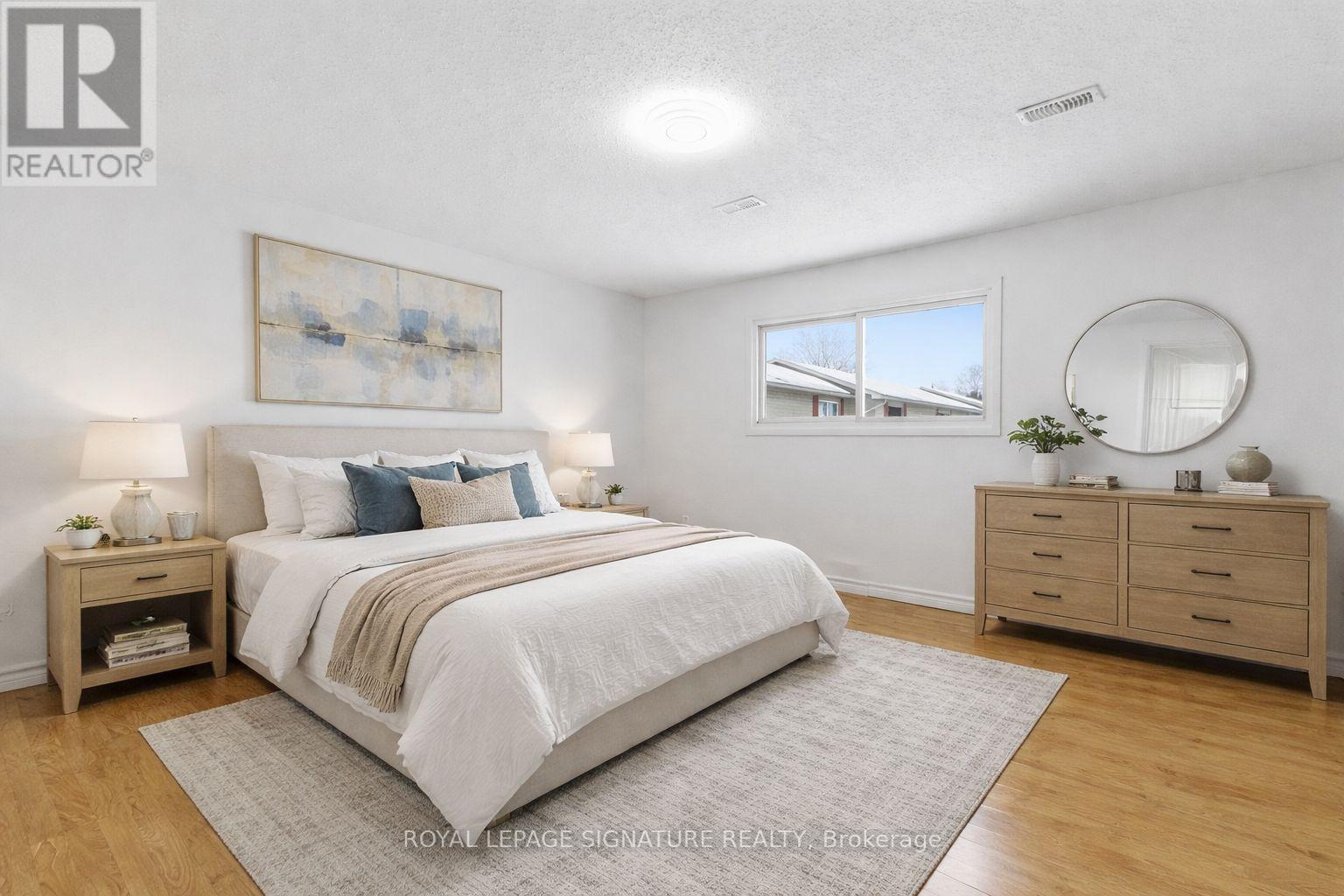 A bedroom with a large bed, a nightstand with a lamp, and a round mirror on the wall.