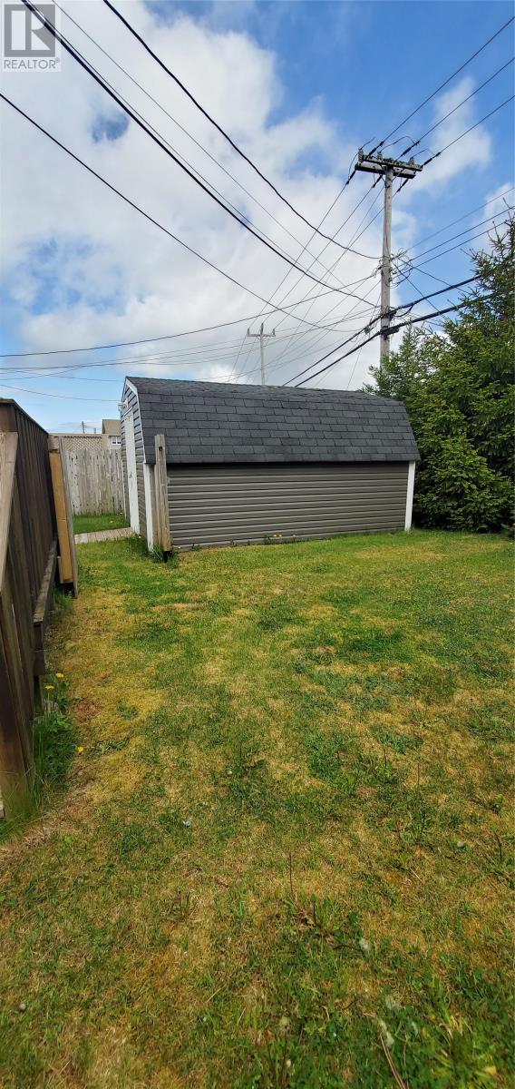 A shed sits in a grassy yard with a wooden fence and power lines in the background.