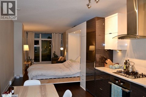 A modern bedroom with a bed, a table, and a kitchen area.