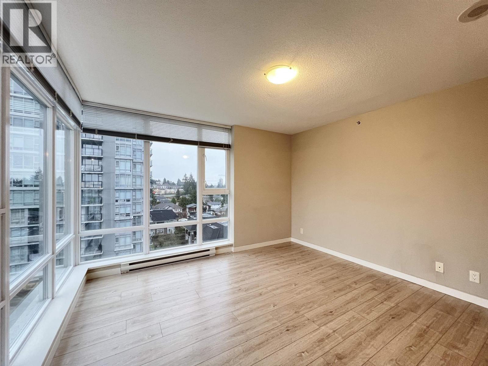 A spacious room with wooden flooring and large windows overlooking a cityscape.