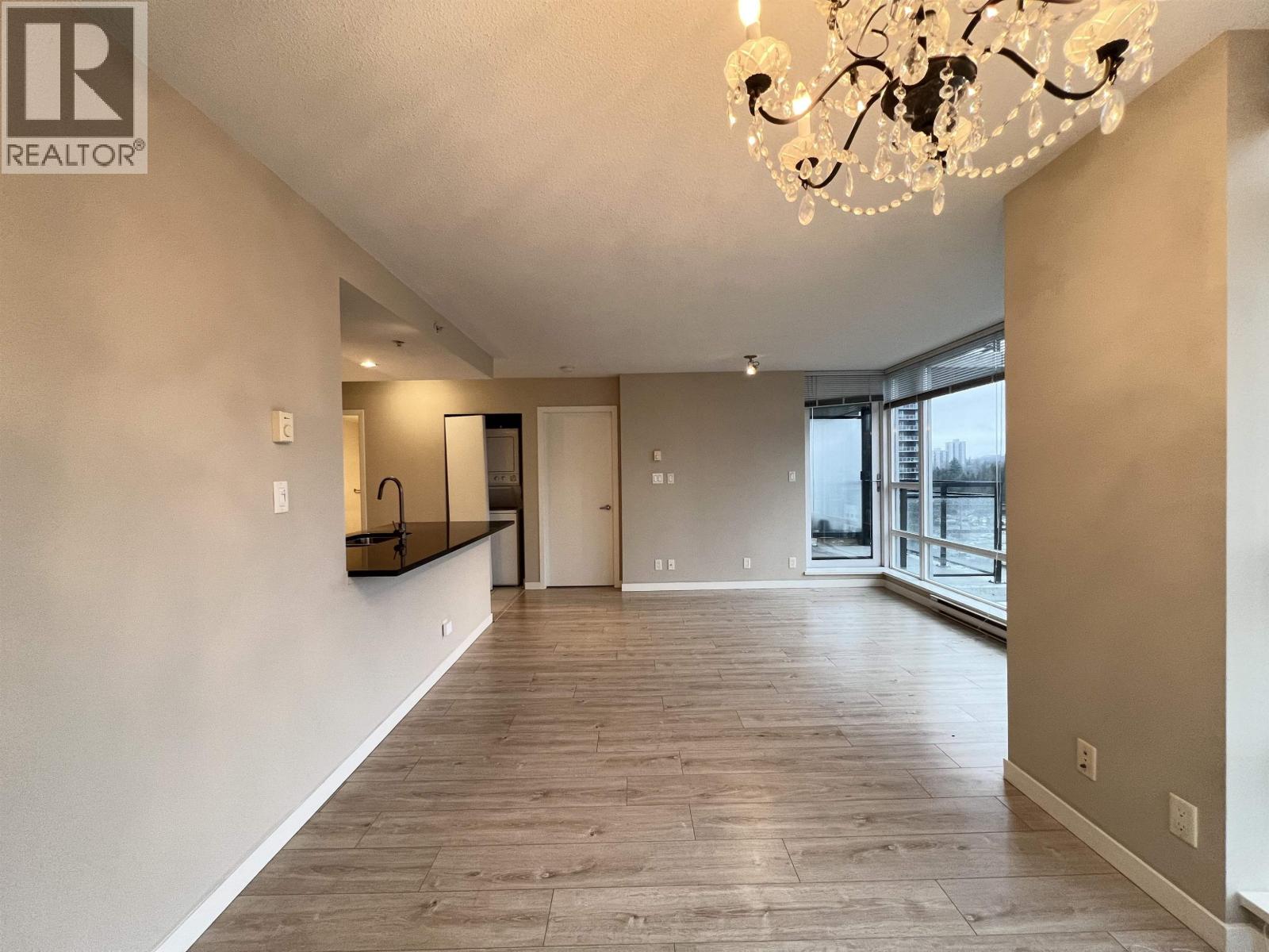 A large, empty room with a chandelier and hardwood floors.