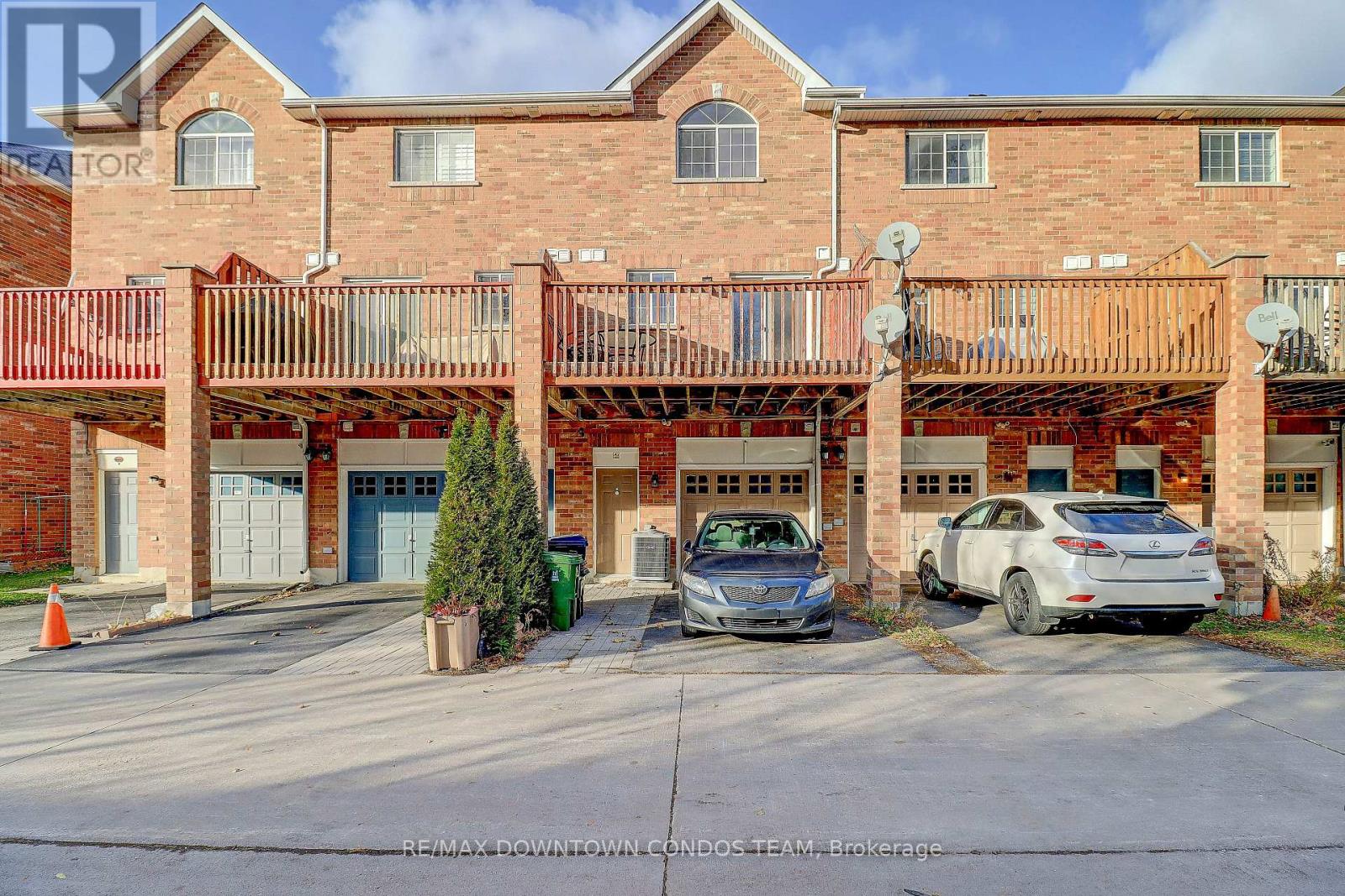 A brick building with a balcony and two cars parked in front.