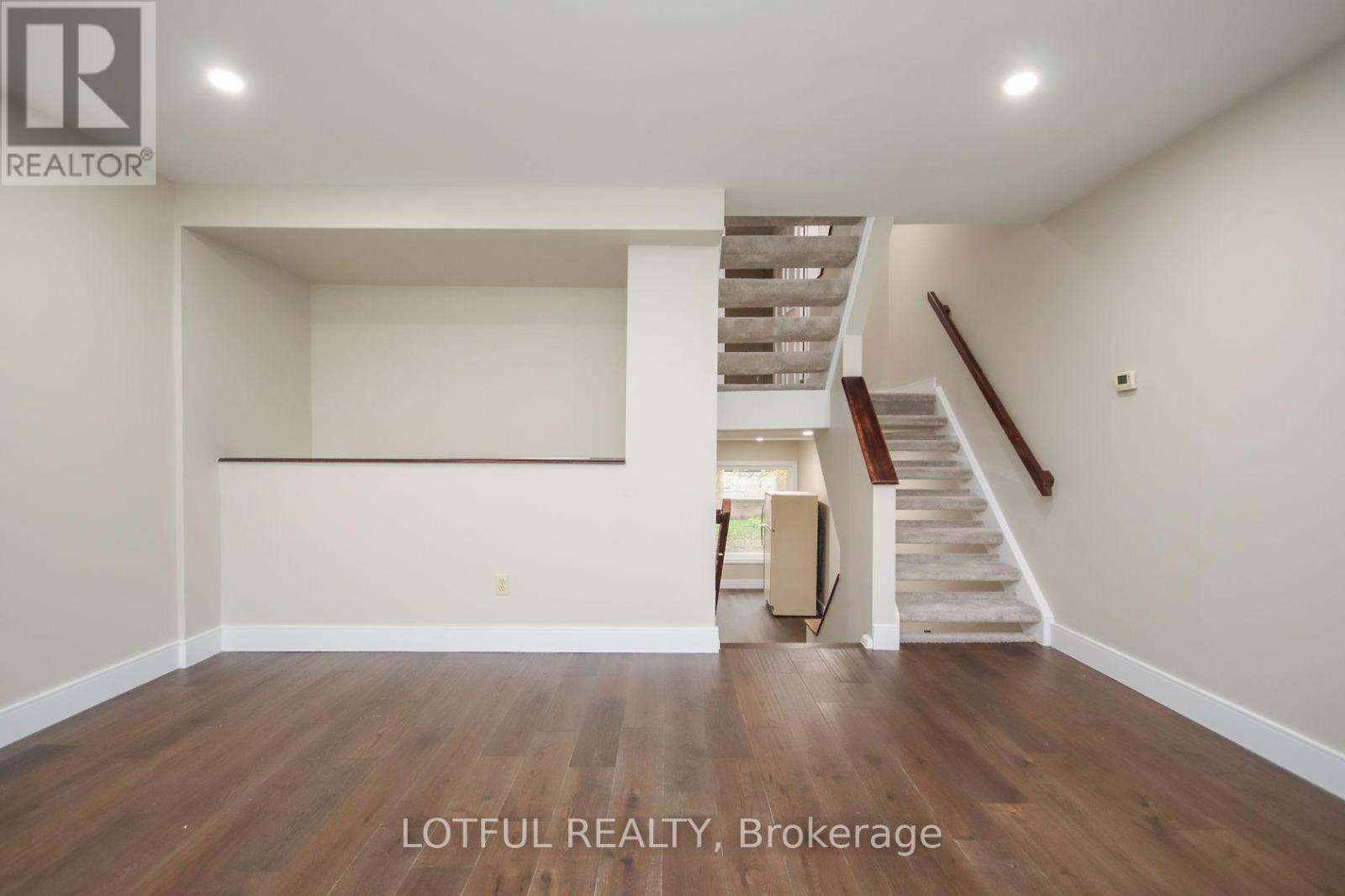 A spacious room with wooden floors and a staircase leading to another level.