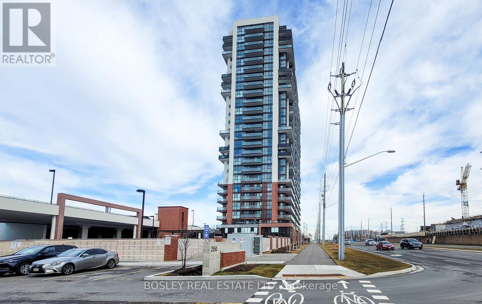 A tall building with a glass facade stands in the middle of a street with cars parked on the side.