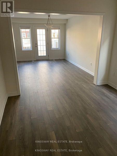 A room with wooden flooring and a large doorway leading to another room.