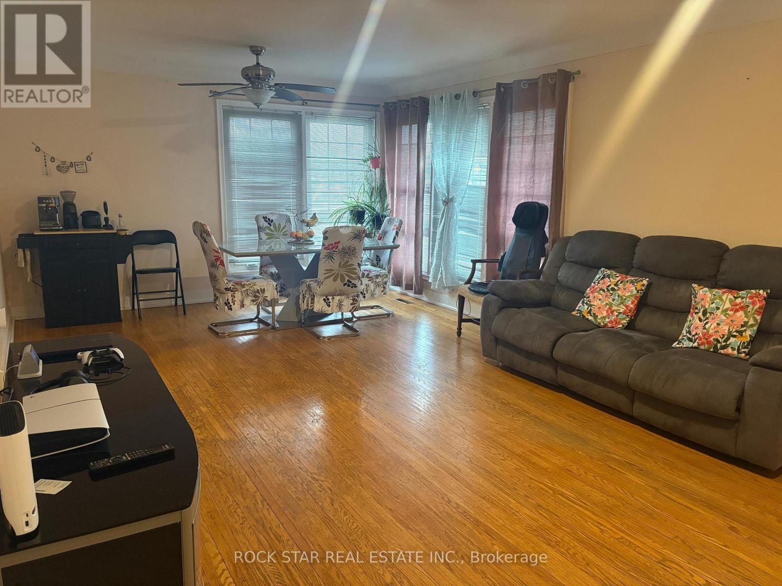 A living room with a black couch, a dining table with chairs, and a ceiling fan.