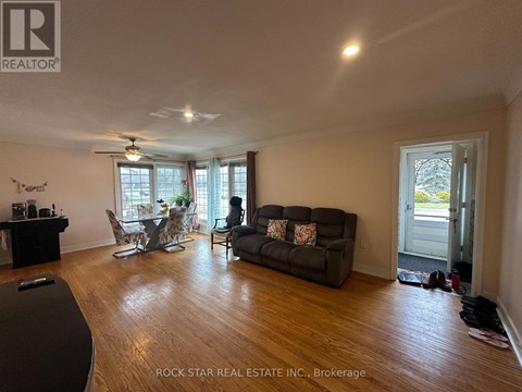 A living room with a black couch, a dining table with chairs, and a ceiling fan.