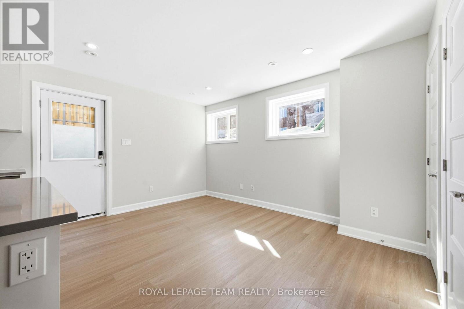 A spacious room with light wood flooring and white walls, with a door on the left and a picture on the wall.