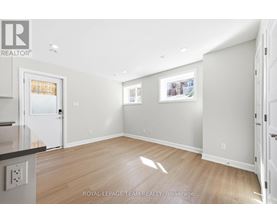 A spacious room with light wood flooring and white walls, with a door on the left and a picture on the wall.